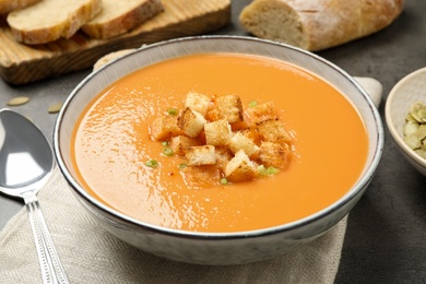 Tasty creamy pumpkin soup with croutons in bowl on grey table
