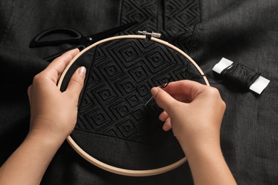 Woman embroidering black shirt with thread in hoop, above view. Ukrainian national clothes