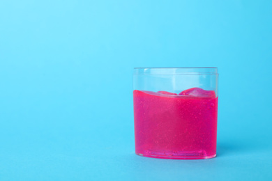 Photo of Pink slime in plastic container on light blue background. Space for text