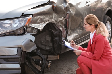 Photo of Insurance agent filling claim form near broken car outdoors