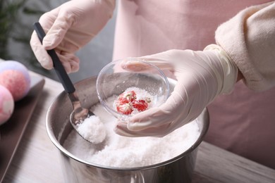 Woman in gloves making bath bomb at wooden table indoors, closeup