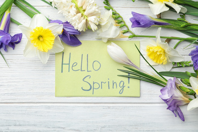 Card with words HELLO SPRING and fresh flowers on white wooden table, flat lay