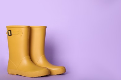 Yellow rubber boots on violet background. Space for text