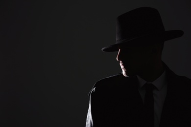 Old fashioned detective in hat on dark background. Space for text