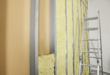 Ladder near wall with metal studs and insulation material indoors