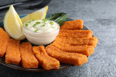 Fresh breaded fish fingers, sauce and lemon served on grey table, closeup