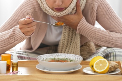 Sick young woman eating soup to cure flu at home, closeup