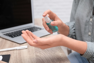 Office employee applying hand sanitizer at workplace, closeup