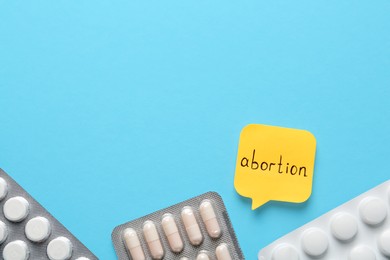 Paper note with word Abortion and pills on light blue background, flat lay. Space for text