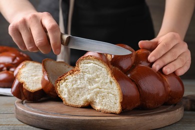 Woman cutting homemade braided bread at wooden table, closeup. Challah for Shabbat