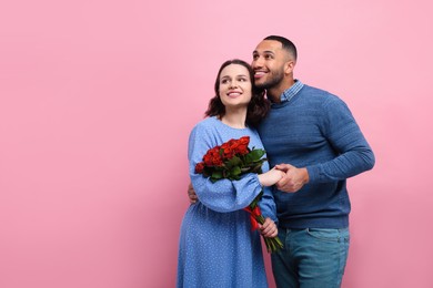 Photo of Happy couple celebrating Valentine's day. Beloved woman with bouquet of red roses on pink background, space for text