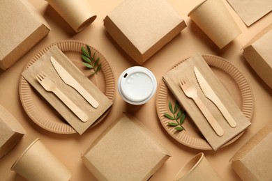 Paper and wooden tableware with green twigs on beige background, flat lay. Eco friendly lifestyle