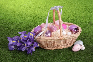 Photo of Easter basket with painted eggs and iris flowers on green grass