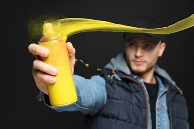 Handsome man spraying yellow paint against black background