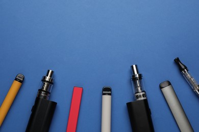 Many electronic smoking devices on blue background, flat lay. Space for text