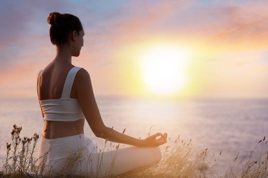Woman meditating near sea at sunset. Practicing yoga