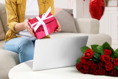 Photo of Valentine's day celebration in long distance relationship. Woman holding gift box while having video chat with her boyfriend via laptop indoors, closeup