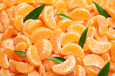 Photo of Fresh juicy tangerine segments with green leaves as background, top view