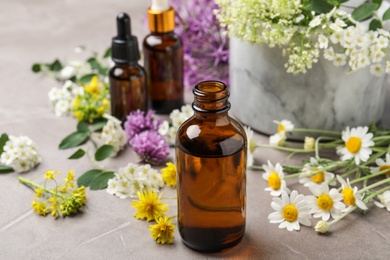 Composition with bottles of essential oils with flowers on grey table