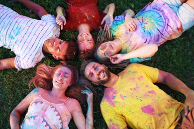 Happy friends covered with colorful powder dyes on green grass outdoors, above view. Holi festival celebration