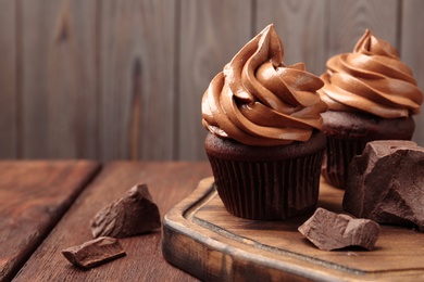 Photo of Delicious cupcakes with cream and chocolate pieces on wooden table, closeup