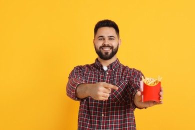 Young man with French fries on orange background, space for text