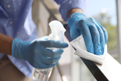 Woman in latex gloves cleaning railing with wet wipe and detergent indoors, closeup