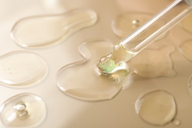 Dripping hydrophilic oil from pipette on beige background, closeup