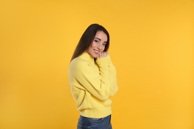 Beautiful young woman wearing warm sweater on yellow background