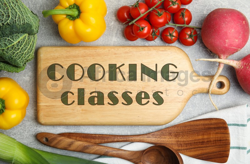 Wooden board with inscription Cooking Classes and different fresh vegetables on light grey table, flat lay