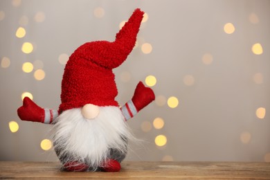 Cute Christmas gnome on wooden table against blurred festive lights. Space for text