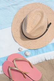 Beach towel with straw hat, seashells and flip flops on sand, flat lay