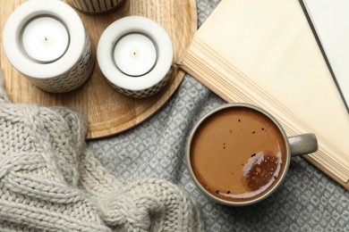 Cup of delicious hot winter drink and candles on grey fabric, flat lay. Winter drink