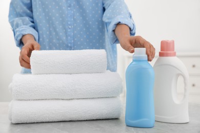 Photo of Woman with bottles of detergents and clean towels at light grey marble table, closeup