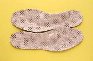 Beige orthopedic insoles on yellow background, flat lay
