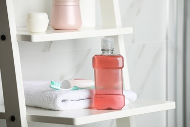 Bottle of mouthwash, toothpaste and brush on white shelf indoors