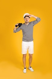 Serious sailor man with binoculars on yellow background