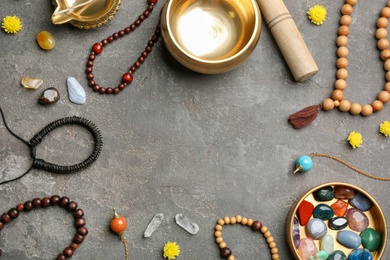 Frame of golden singing bowl and healing stones on grey table, flat lay with space for text