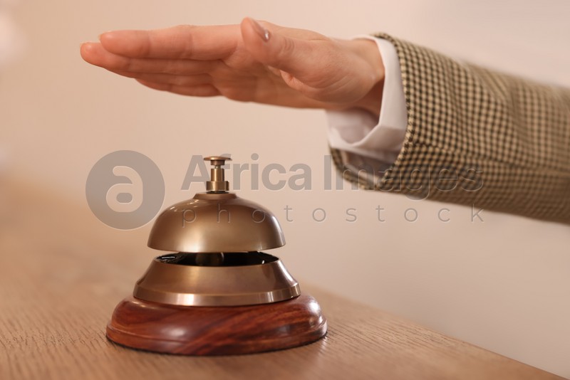 Photo of Woman ringing hotel service bell at wooden reception desk, closeup