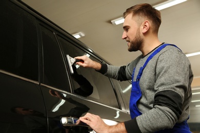 Skilled worker washing tinted car window in shop