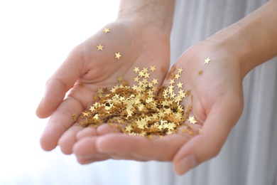 Woman holding gold confetti stars on light background, closeup. Christmas celebration