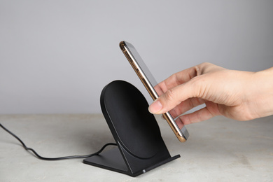Woman putting mobile phone onto wireless charger at  grey table, closeup