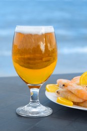 Photo of Cold beer in glass and shrimps served with lemon on beach, closeup