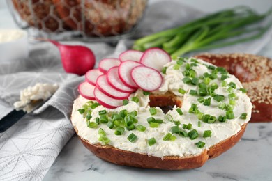 Delicious bagel with cream cheese, radish and green onion on white marble table, closeup