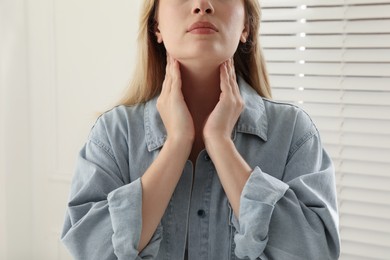 Young woman doing thyroid self examination near window indoors, closeup
