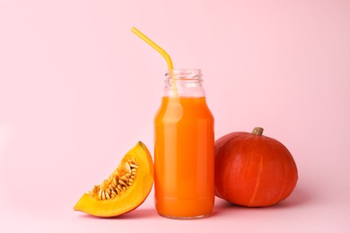 Photo of Tasty pumpkin juice in glass bottle, whole and cut pumpkins on pink background