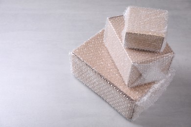 Photo of Cardboard boxes covered with bubble wrap on light grey table. Space for text