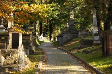 View of cemetery with granite tombstones and paved footpath on sunny day. Funeral ceremony