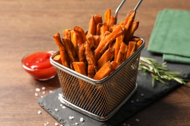 Photo of Frying basket with sweet potato fries on wooden table, closeup