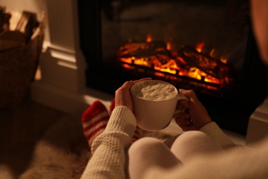 Photo of Woman holding drink near fireplace with burning woods indoors, closeup